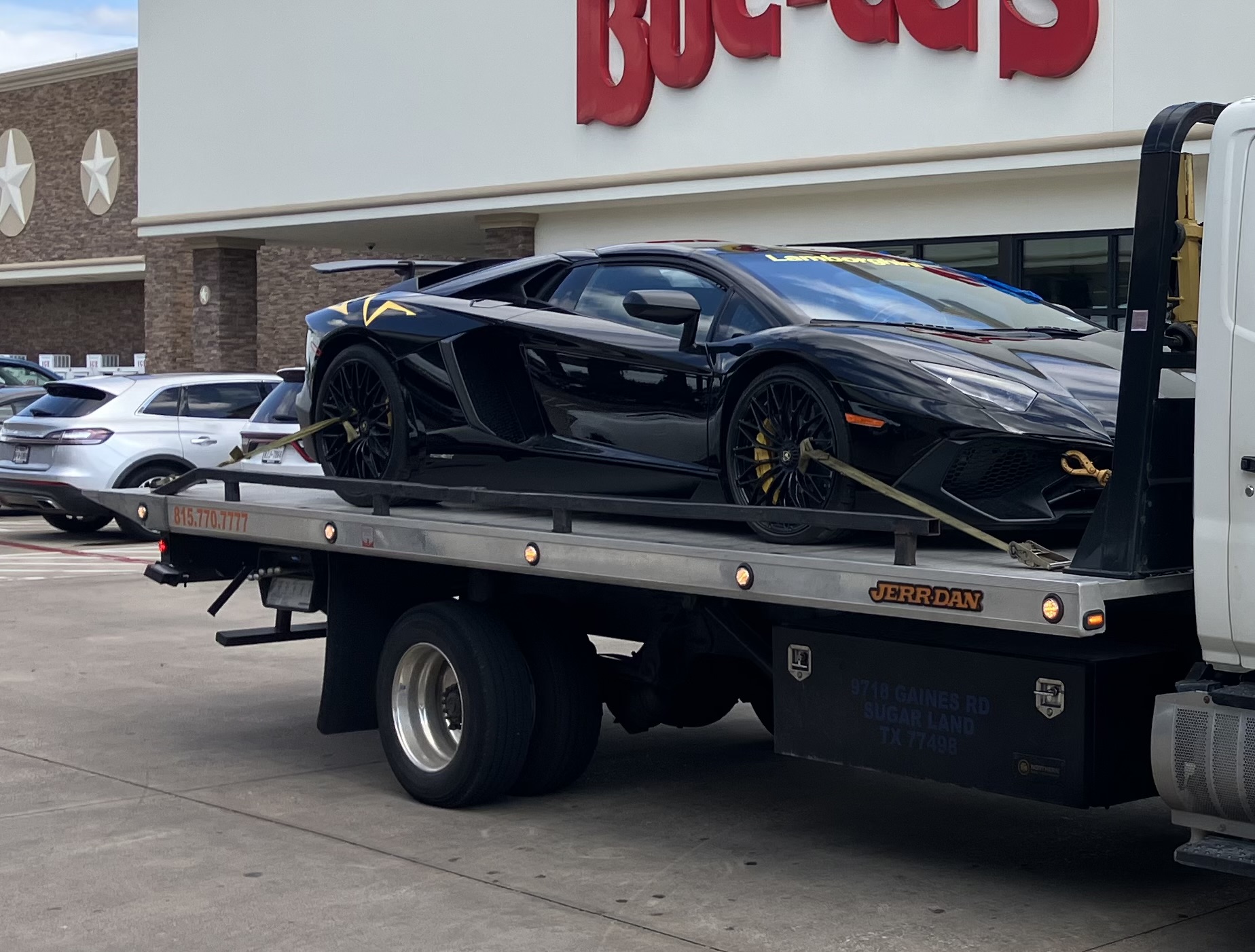 Black luxury sports car secured on a tow truck outside a Bucees store